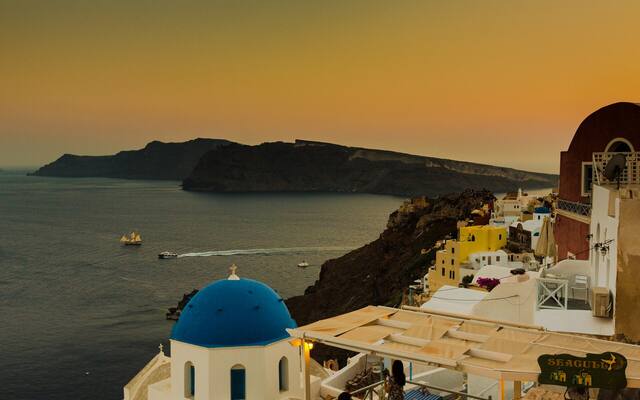 Oia bij zonsondergang met een blauwe koepel en de caldera op de achtergrond