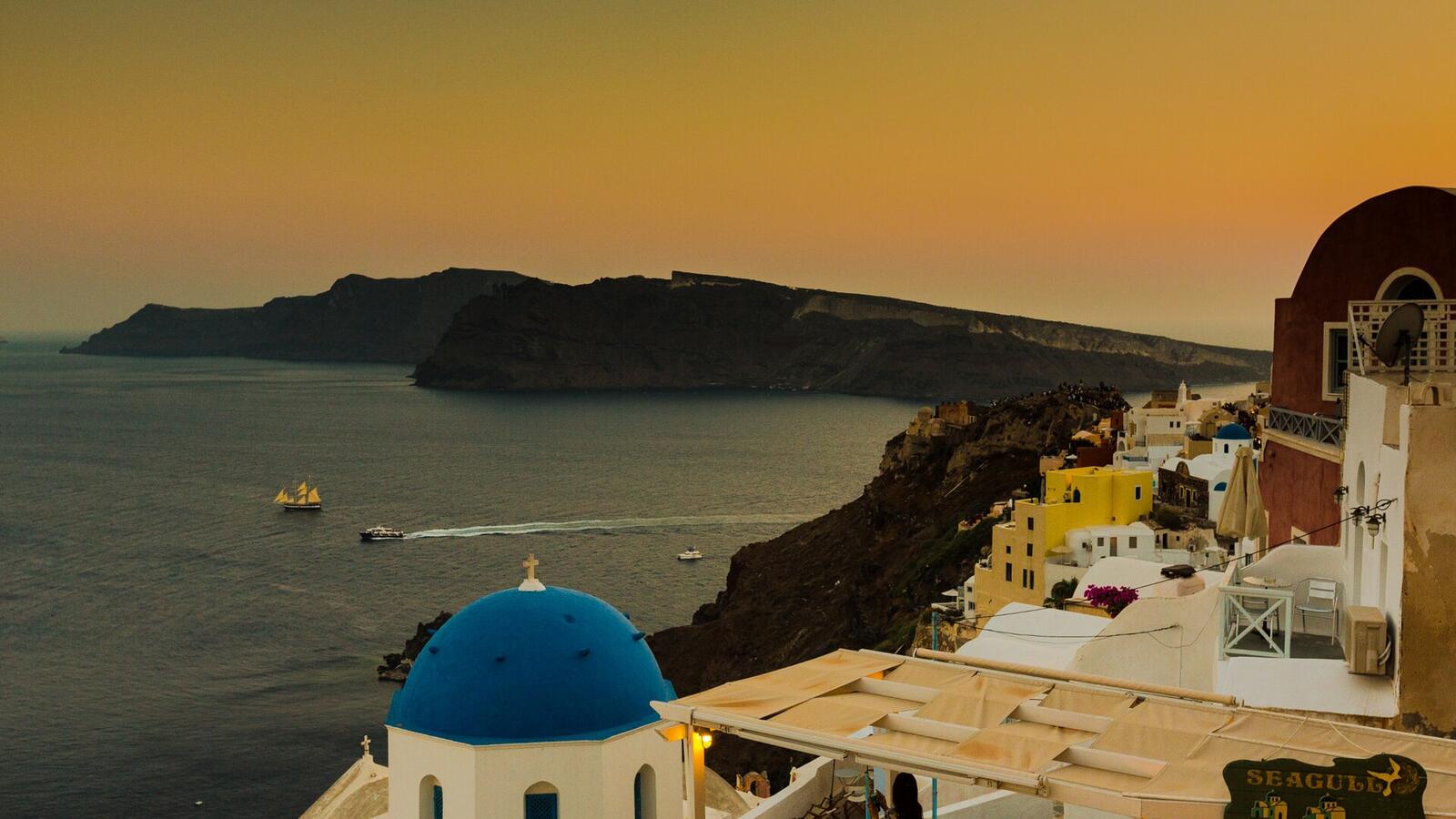 Oia bij zonsondergang met een blauwe koepel en de caldera op de achtergrond