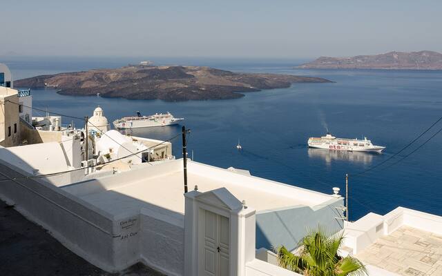 Witte terrassen in Fira met uitzicht over de caldera en een cruiseschip in de verte