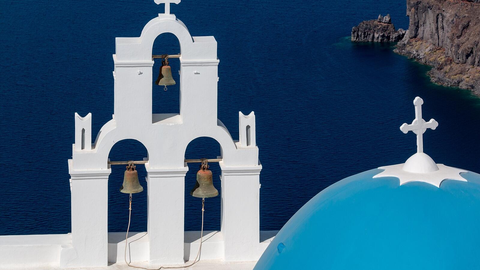 De drie klokken van de kerk in Firostefani met een blauwe koepel boven de caldera