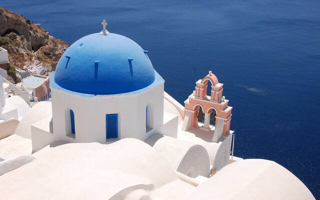 Een kerk met een blauwe koepel en een roze klokkentoren in Oia boven de caldera