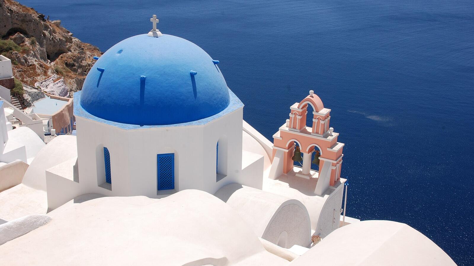 Een kerk met een blauwe koepel en een roze klokkentoren in Oia boven de caldera