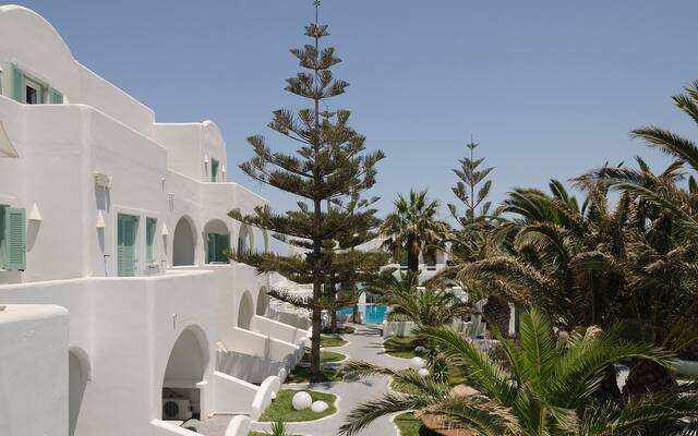 Hotel met witte gebouwen, palmbomen en een zwembad in Fira